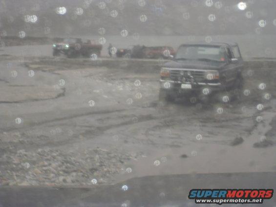 Dark SUV with a prominent grille and front bumper, stuck in mud