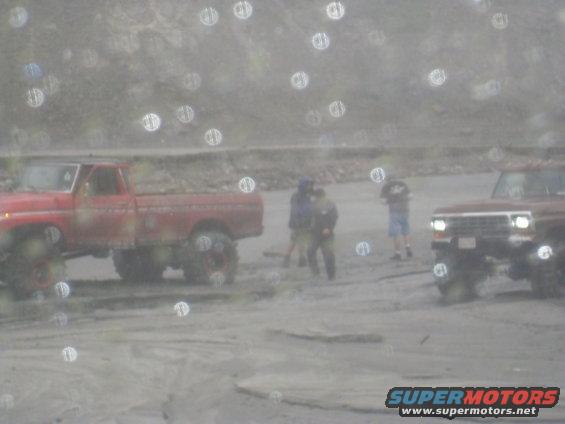 Red pickup truck and maroon SUV in a sandy, outdoor area with people