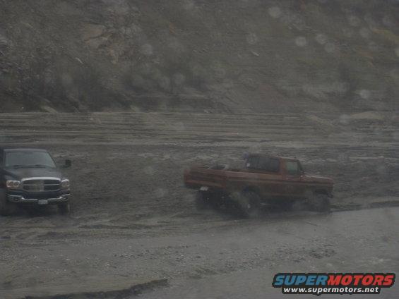 red pickup truck and black pickup truck driving on a muddy road