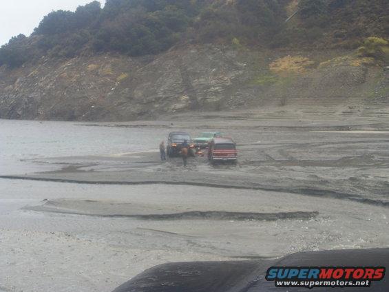 Red 1978 Ford Bronco and other SUVs stuck in mud near a rocky hill