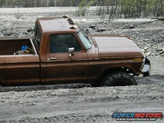 Brown pickup truck stuck in mud, side view. Visible Supermotors.net logo