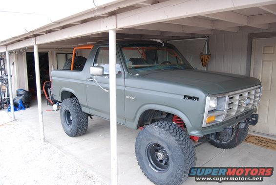Green Ford Bronco with off-road tires parked under a carport