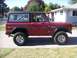 1970 Ford Bronco - A red 1970 Ford Bronco is seen from the side, parked in a residential driveway.