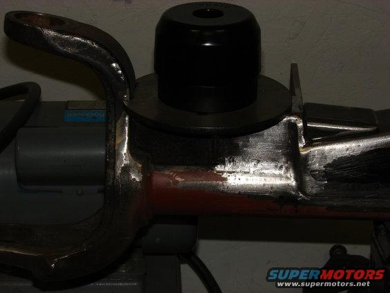 Close-up of a metal suspension component with a black rubber bushing on top, mounted on machinery