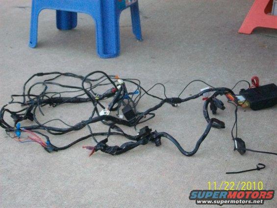 Vehicle wiring harness spread on concrete, with a blue plastic stool in the background