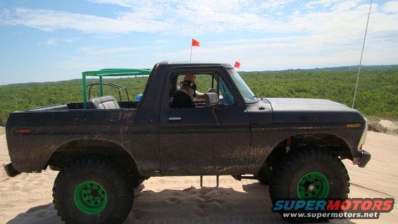 Side view of a dark 1979 Ford Bronco with a green roll cage and bright green wheels on sand dunes