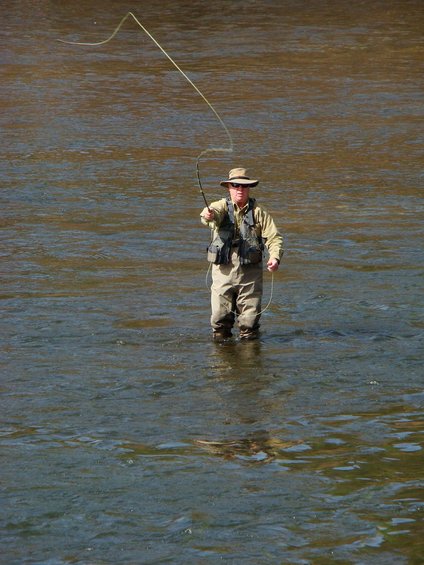 Man in fishing gear casting a line while standing in a river
