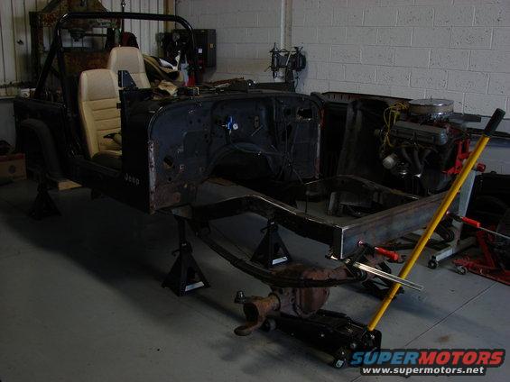 Jeep CJ body and frame on jack stands, engine visible to the right