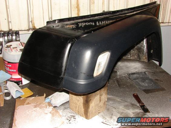 Black Jeep fender with amber marker light, resting on wooden blocks
