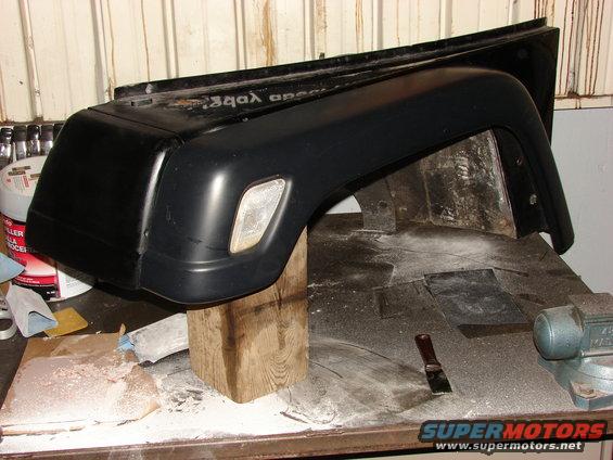 Black Jeep fender and bumper assembly on workbench with tools and supplies