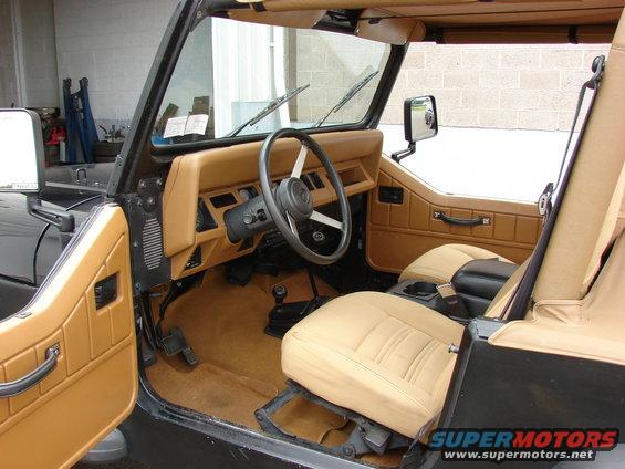 Interior of a Jeep with tan seats and door panels, black steering wheel, and floor shifter
