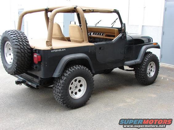 Black 1993 Jeep YJ Wrangler with tan soft top and spare tire on rear bumper, viewed from rear-right