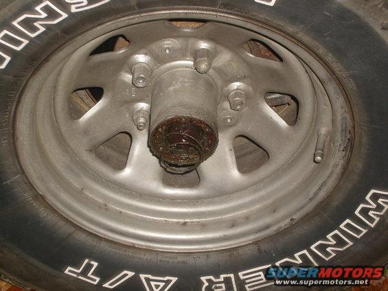 Wheel hub with grease and lug nuts, part of a tire with white lettering