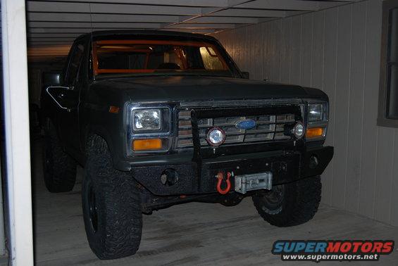 Dark gray Ford truck with orange roll cage, aftermarket bumper, and winch