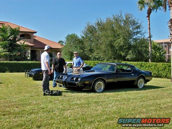 1977 Pontiac Trans Am parked on grass with three men nearby; another black car is visible behind it