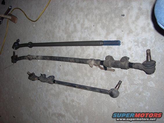 Three steering linkage rods laid out on a concrete floor