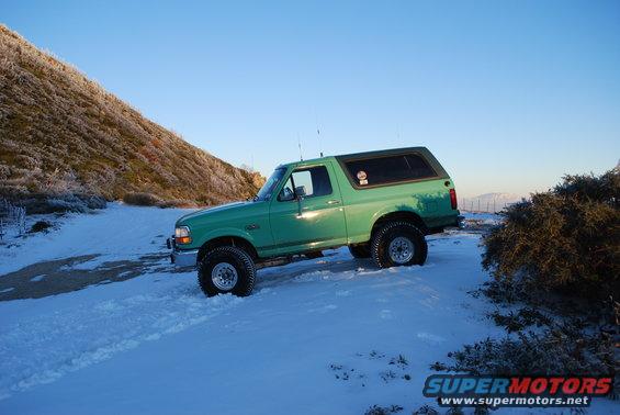 Green 1996 Ford Bronco with aftermarket wheels parked in snow, side view
