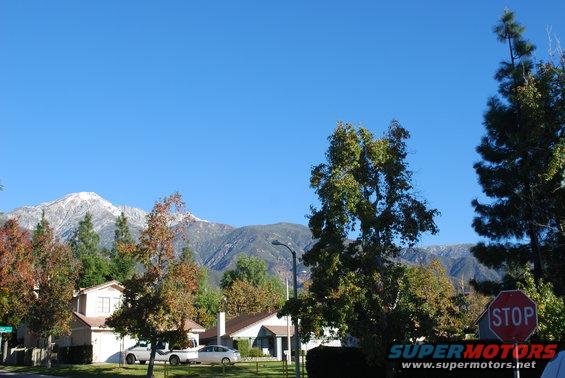 White pickup truck and two cars parked on a street with houses and mountains behind them