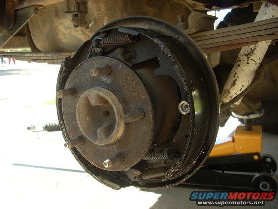 Rear drum brake assembly with brake shoes and springs visible, supported by a jack