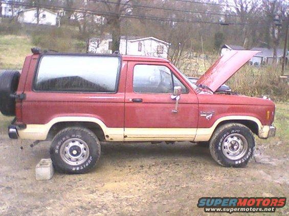 Red 1986 Ford Bronco II parked on dirt, hood up, spare tire on back