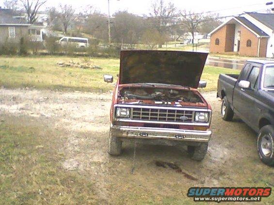 Red SUV with hood open, front view, showing engine and grille. Muddy ground