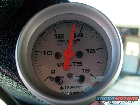Close-up of Auto Meter voltmeter gauge with red needle pointing to 13.5 volts