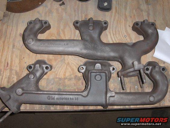 Two cast iron exhaust manifolds with GM part numbers visible