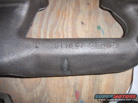 Close-up of a cast iron exhaust manifold with stamped markings including '2', 'F10 OT', and '14CON4'