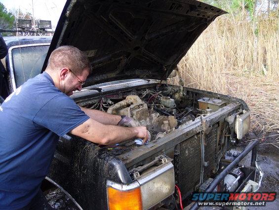 Mud-covered truck engine compartment with man working on it. Hood is open
