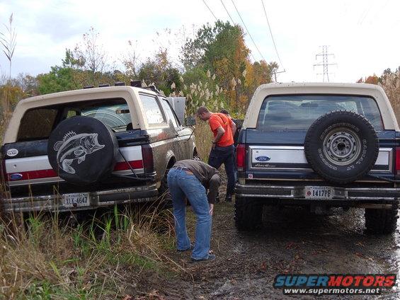Two 1985 Ford Broncos stuck in mud, one with a bass fish spare tire cover