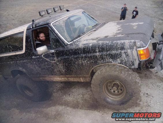 Mud-covered black Ford Bronco with a white top, seen from the front-right