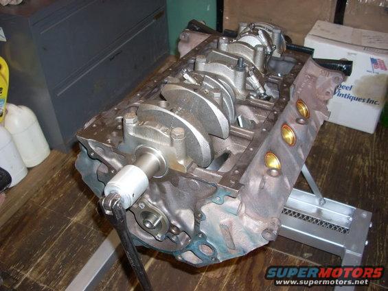 Engine block with crankshaft installed, on a stand. A wrench is attached to the crankshaft