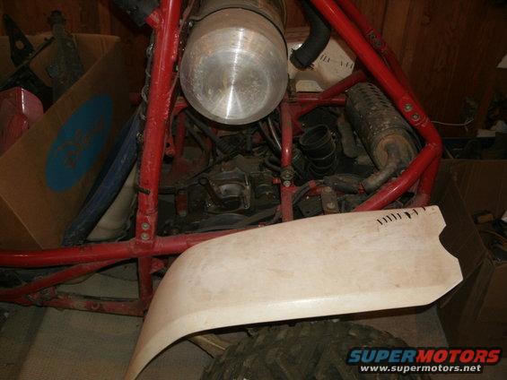Red tubular frame surrounds a metal tank and engine components of an off-road vehicle. A white fender is in the foreground