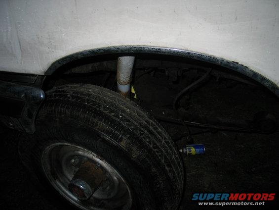 Close-up of rear wheel well with shock absorber and tire visible. Can of lubricant on the ground