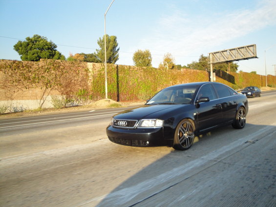 Black Audi sedan with aftermarket wheels driving on a highway