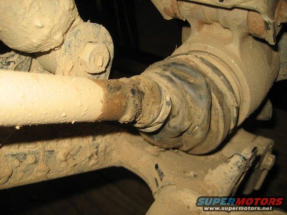 Mud-covered drivetrain component, possibly a CV joint or driveshaft, with visible grease and metal parts