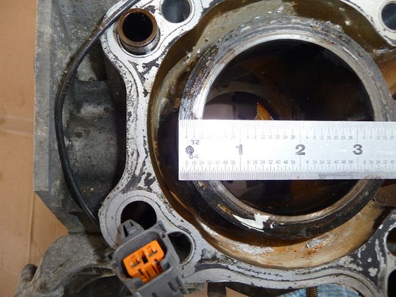 Engine block cylinder bore being measured with a ruler. Orange electrical connector visible