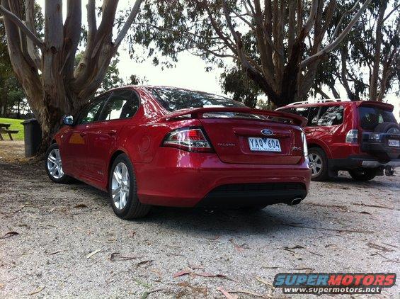 Rear view of red Ford Falcon sedan parked next to a red SUV. License plate YAQ 604