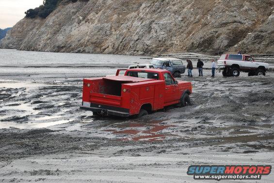 Red pickup truck with toolboxes stuck in mud, rear view
