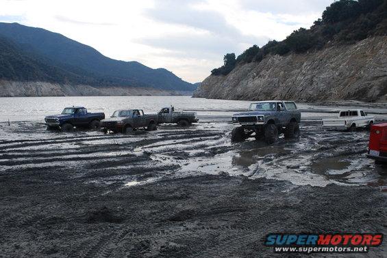 Gray Ford Bronco with large tires on muddy ground near water