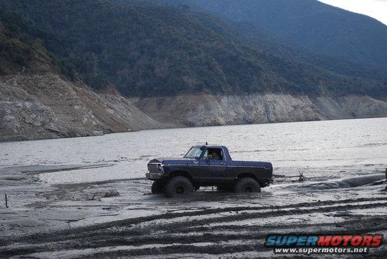 Blue lifted 1978 Ford F-150 driving through mud near a lake