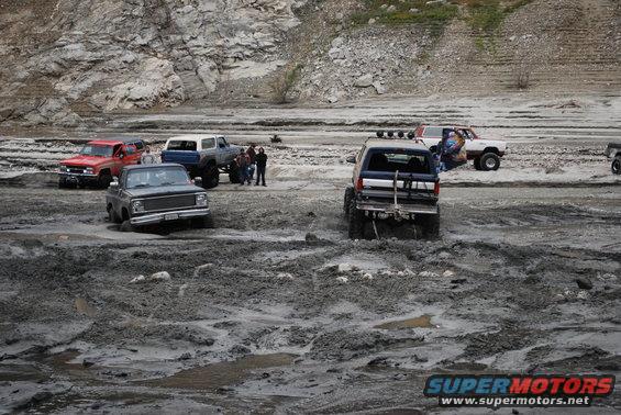 Several off-road vehicles stuck in mud, with rocky hills in the background