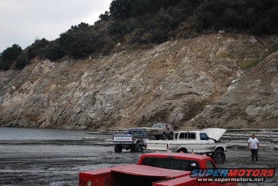 White 1978 Ford Bronco with hood open, parked on muddy ground near water