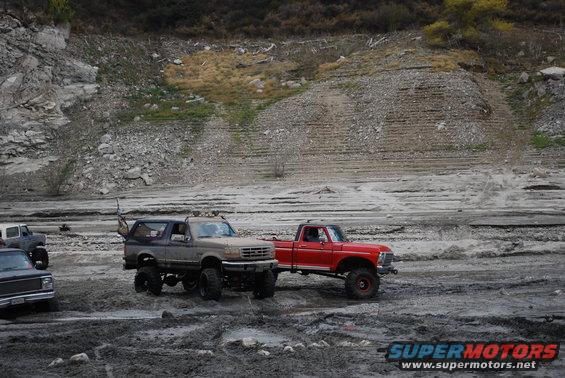 Blue lifted Bronco and red pickup truck on muddy ground