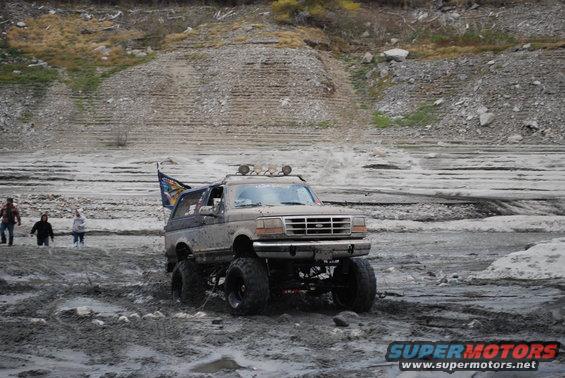 Lifted 1996 Ford Bronco driving through mud with a flag on the back