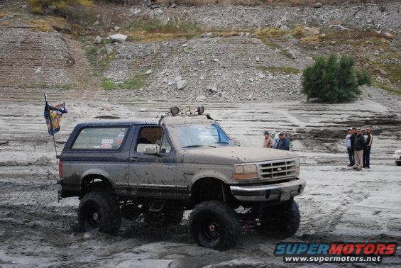 Lifted 1996 Ford Bronco driving through mud with a flag on the back
