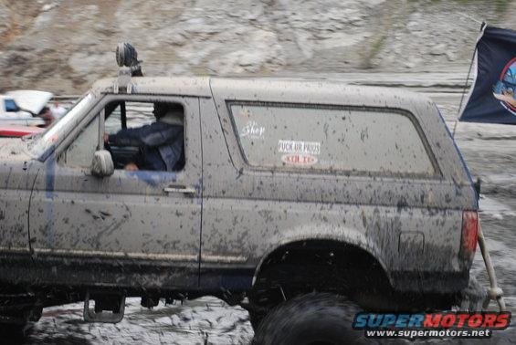 1996 Ford Bronco covered in mud, driving off-road with a flag on the back