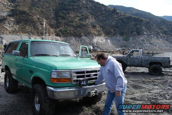 Green Ford Bronco with a winch on the front bumper, parked on a dirt lot with a man inspecting it