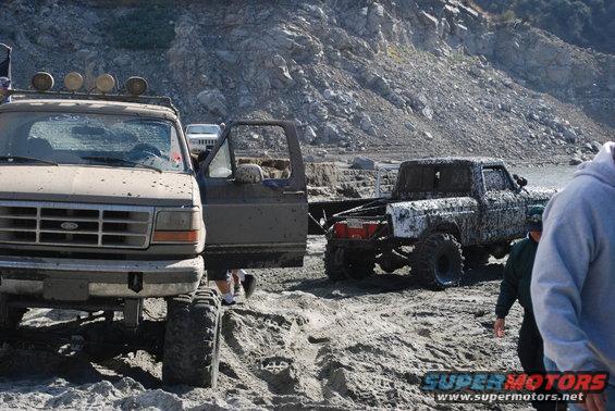 Muddy Ford truck with open door, another muddy truck behind it, rocky terrain