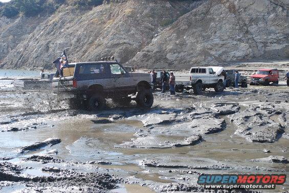 Gray Ford Bronco with lifted suspension splashing mud, seen from the front-left